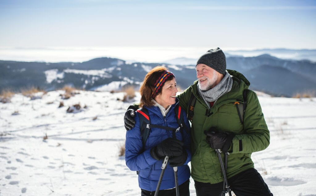 Senior couple hikers with nordic walking poles in snow-covered winter nature