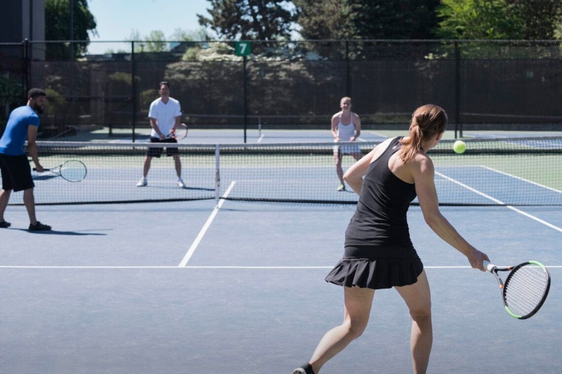 Four people playing tennis on outdoors court, a woman playing a forehand shot.