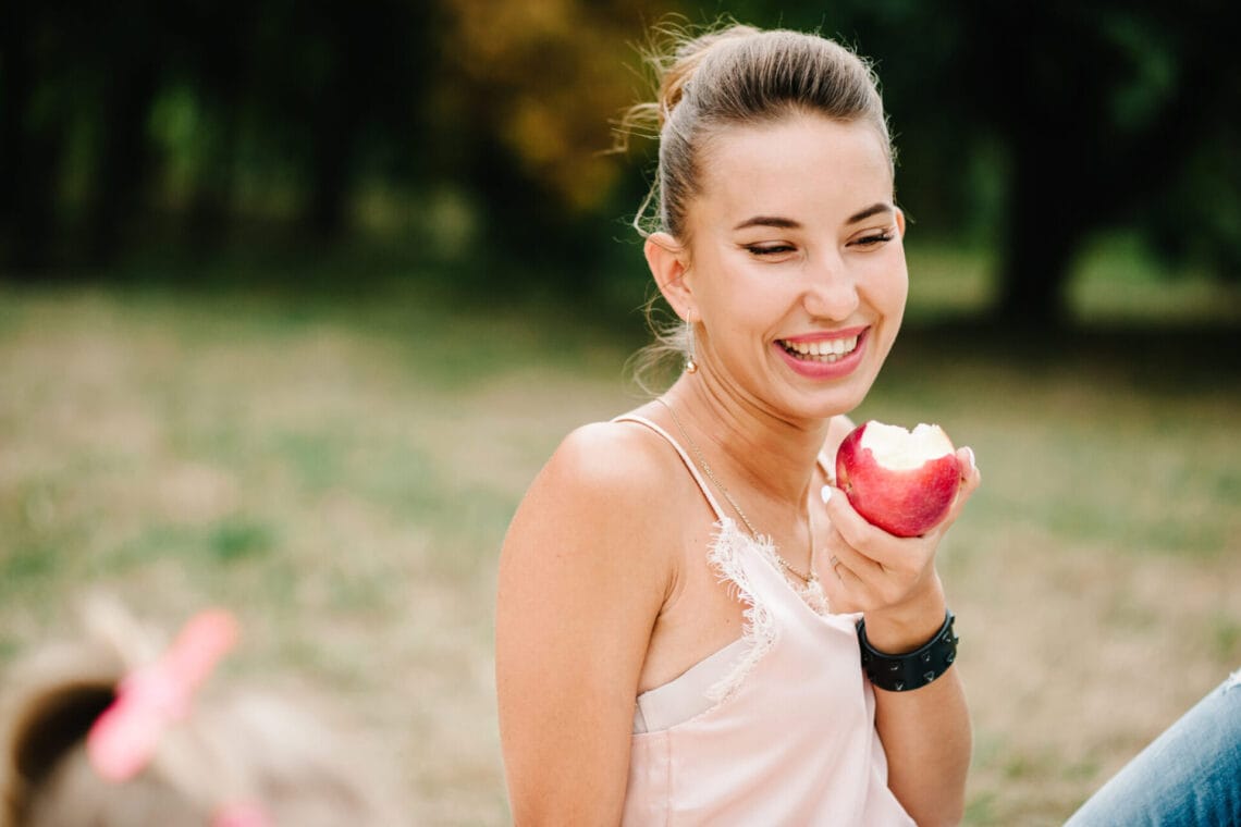 Girl eating apples on a blanket on a picnic in the summer. Happy family in the park on holidays.