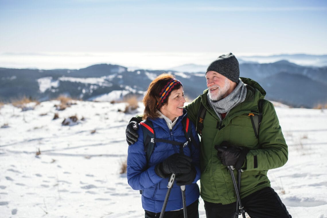 Senior couple hikers with nordic walking poles in snow-covered winter nature