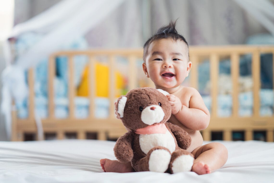 Asian baby sit with teddy bear on ther bed in bedroom